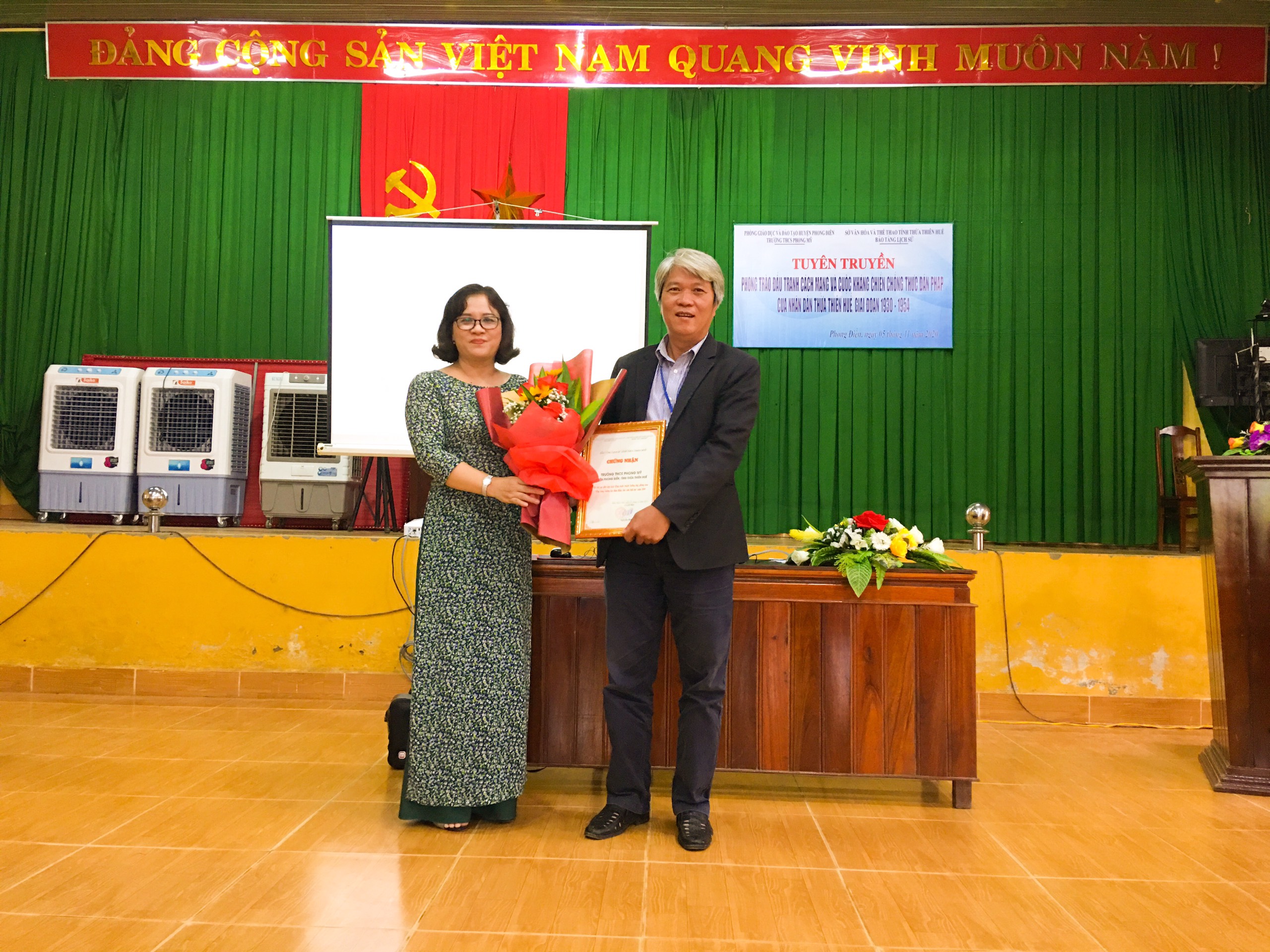 PGĐ Bảo tàng Lịch sử Thừa Thiên Huế trao tặng giấy chứng nhận và hoa cho Hiệu Trưởng THCS Phong Mỹ